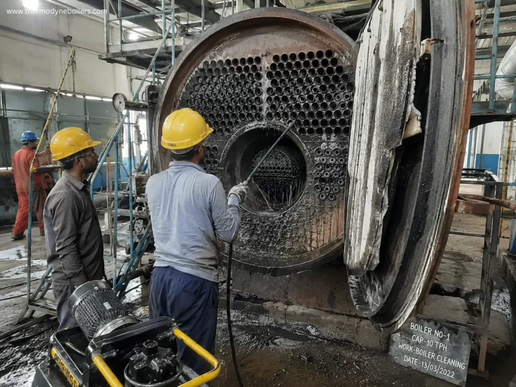 Industrial workers performing mechanical boiler cleaning inside a steam boiler using high-pressure cleaning equipment to remove scale and deposits.
